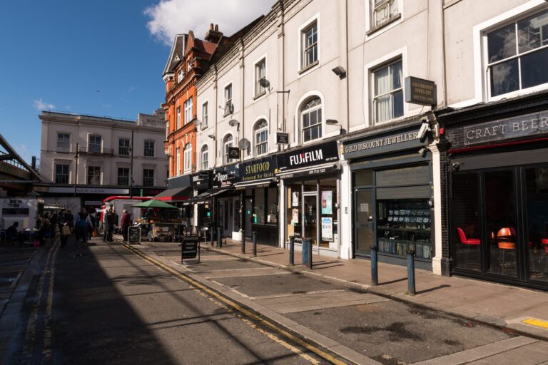 Independent shopfronts along Brixton's Atlantic Road, with pavement traders setting up near the railway arches