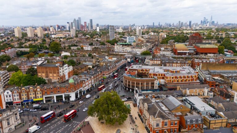 Aerial view of Brixton town centre with red buses on Brixton Road and the City skyline in the distance