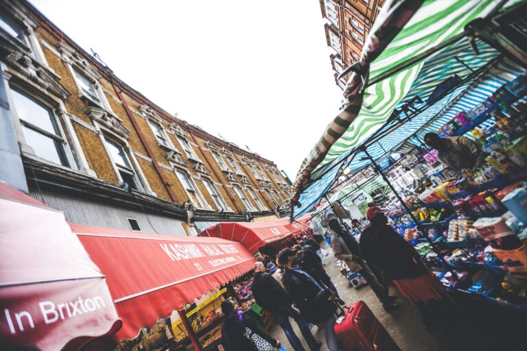 Red and green market awnings on Brixton's Electric Avenue, with the Kashmir Halal Butchers sign visible above the stalls