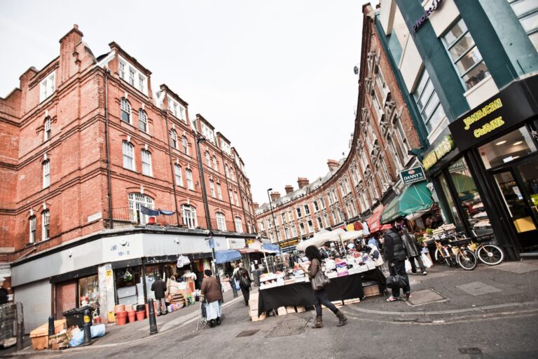 Market traders setting up on a Brixton side street, with Caribbean food shops visible behind the stalls