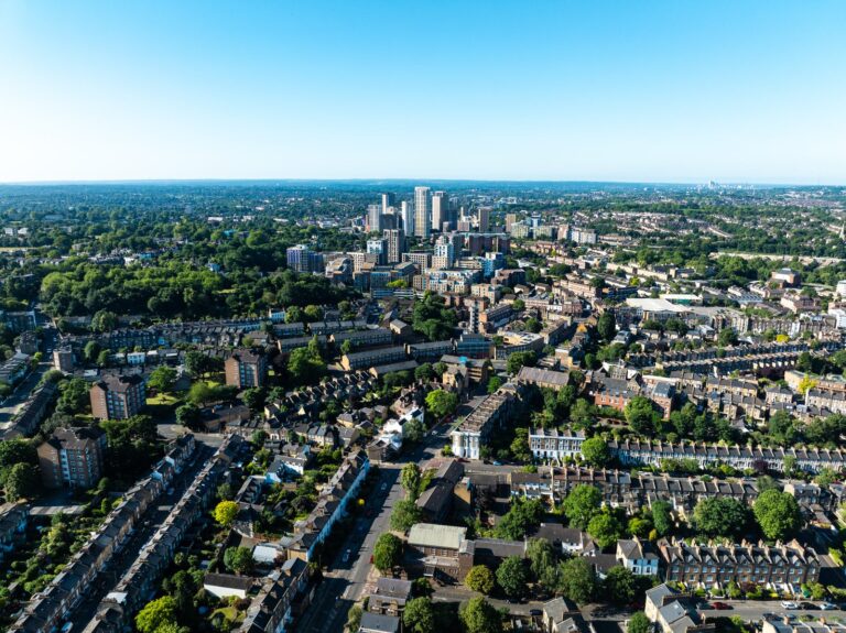 Aerial view over Croydon's residential streets in the foreground, with the modern town-centre towers rising in the middle distance under a clear blue sky