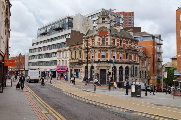 An ornate red-brick Victorian corner building in central Croydon, with pale paving curving across the junction and a mix of modern and Edwardian buildings alongside