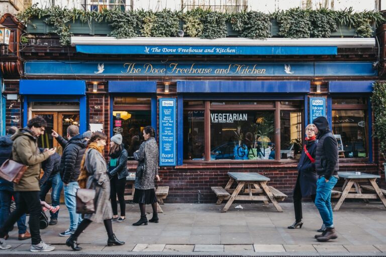 The blue-painted facade of The Dove Freehouse and Kitchen on Broadway Market, with wooden outdoor benches and weekend pedestrians in winter coats passing along the pavement