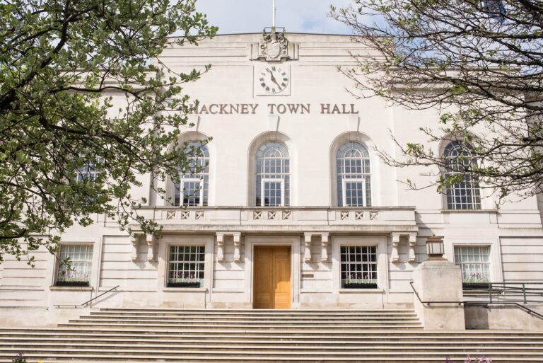 The Art Deco Portland stone facade of Hackney Town Hall on Mare Street, with a central clock and three arched windows above the main entrance steps