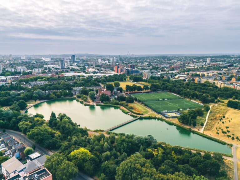 Aerial view of Burgess Park's lake and football pitches, framed by Peckham and Camberwell's residential streets and the wider south London skyline