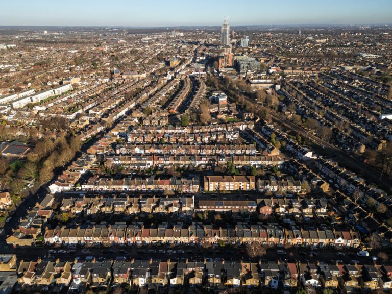 Aerial view over Walthamstow's grid of Victorian terraces in winter afternoon light, with a new-build residential tower rising above the town centre in the middle distance