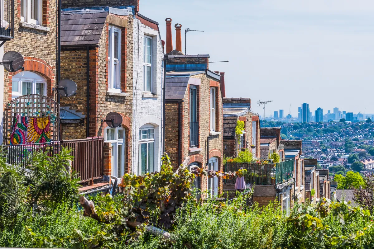 A view across outer London &mdash; rows of residential terraces in the foreground with the central London skyline on the horizon &mdash; in daylight.
